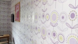 A room with a patterned wallpaper, a wooden bench, and a framed picture on the wall.