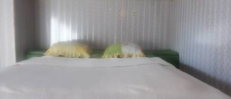 A room with a bed, a green pillow, and a white pillow.