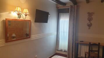 A hotel room with a bed, a desk, a mirror, two wall-mounted lamps, a flat-screen TV, and a window with curtains.