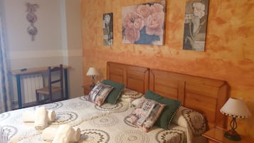 Een slaapkamer met een bed, kussens, een nachtkastje, een lamp, een stoel en een muur met bloemkunst.