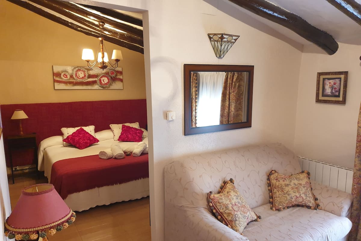 Quarto com cama, mesa de cabeceira, luminária, espelho e um painel decorativo na parede.