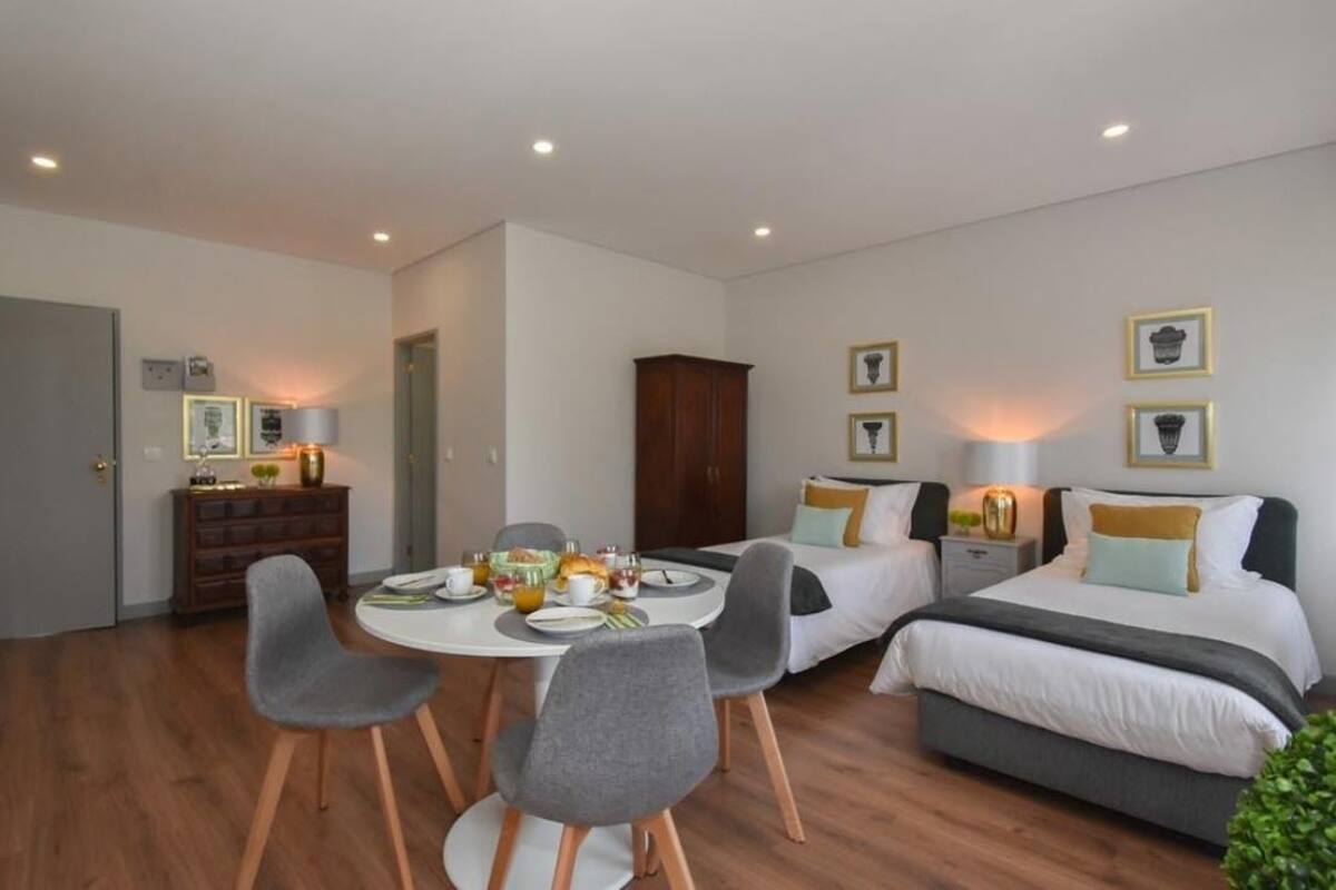 Habitación de hotel con zona de comedor, dos camas individuales, un armario y cuadros en la pared.