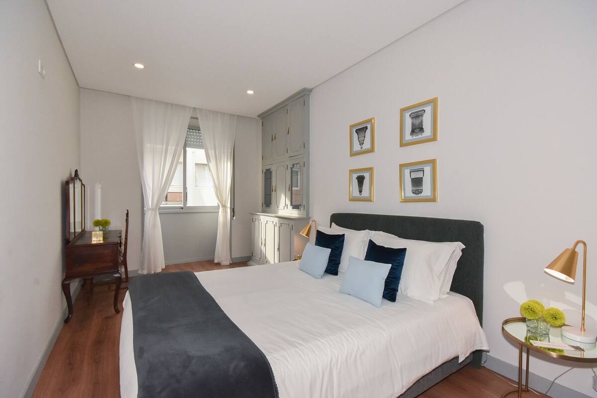 Un dormitorio moderno con una cama grande, una mesita de noche con lámpara y una ventana con cortinas.