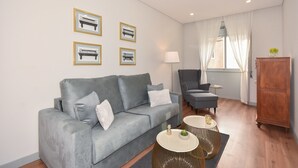 Una sala de estar moderna con un sofá gris, una mesita redonda pequeña, una lámpara y un mueble de madera.