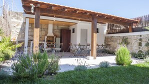 Un edificio de piedra con una pérgola de madera, asientos exteriores y un muro de piedra.