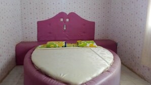 A room with a heart-shaped bed, a purple headboard, and patterned wallpaper.