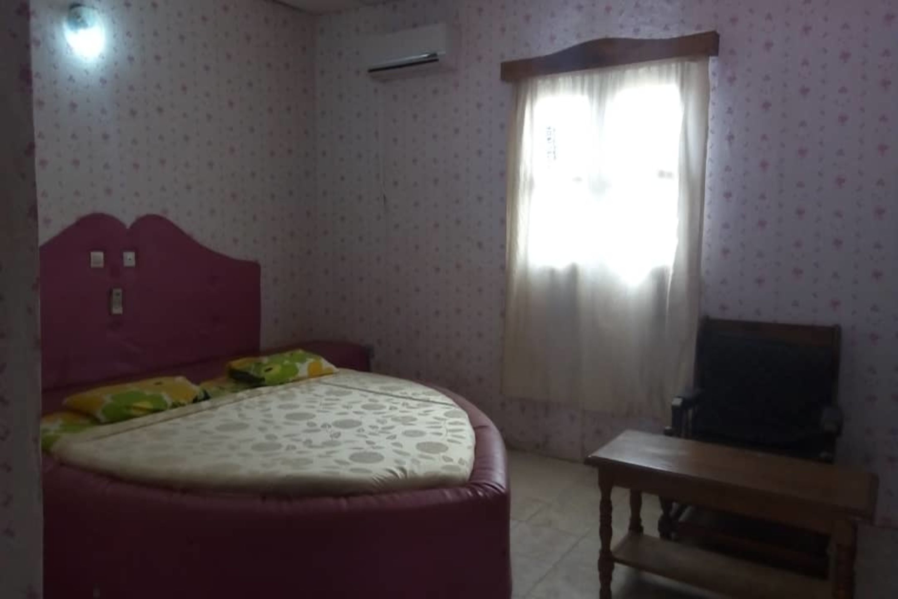 A bedroom with a bed, a wooden nightstand, a desk, and a window with curtains.