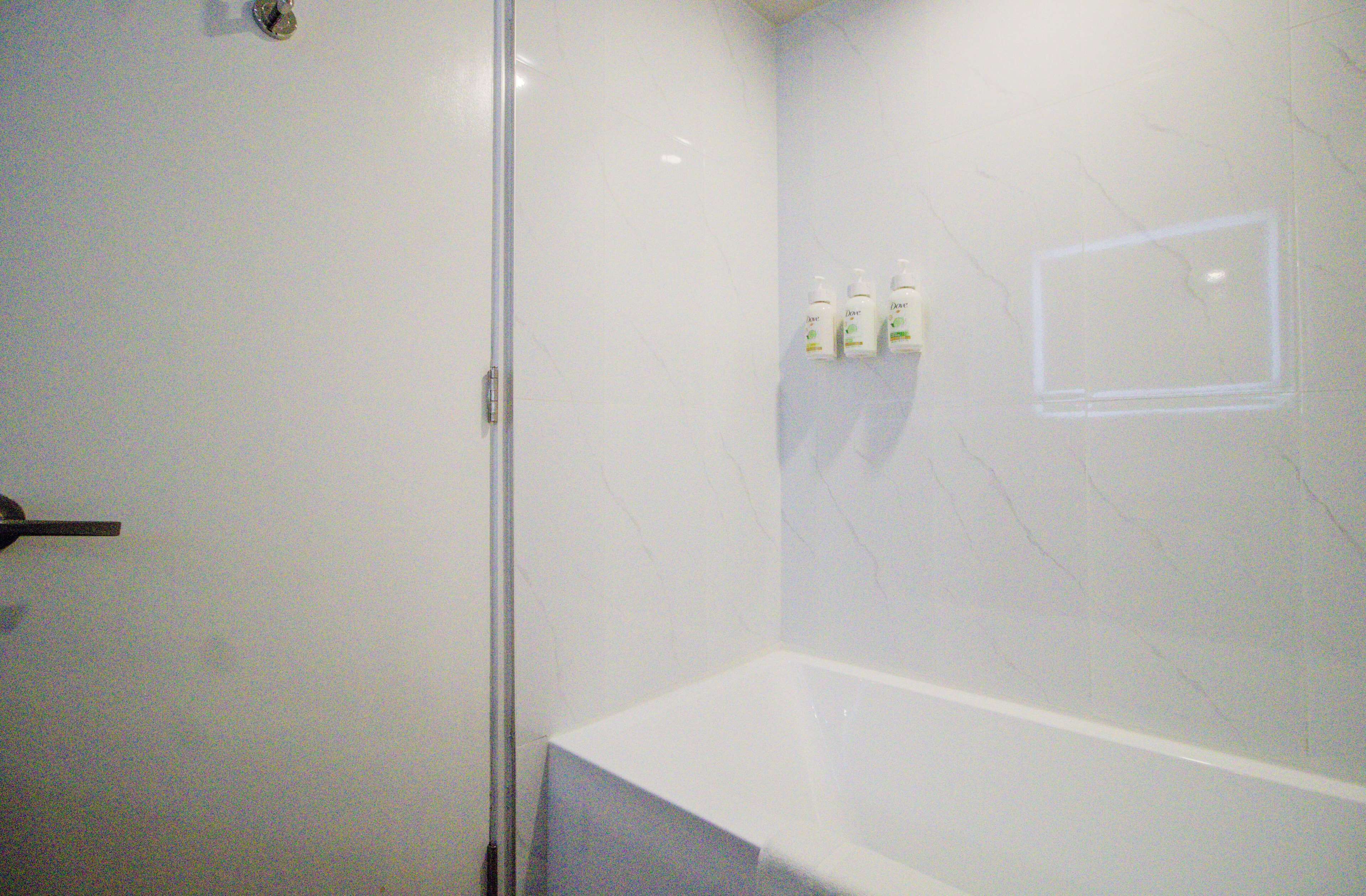 Une salle de bain avec un mur en marbre blanc, une douche en verre et une baignoire blanche.