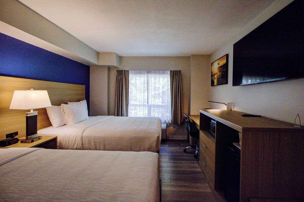 A hotel room with two beds, a desk, a TV, and a window with curtains.