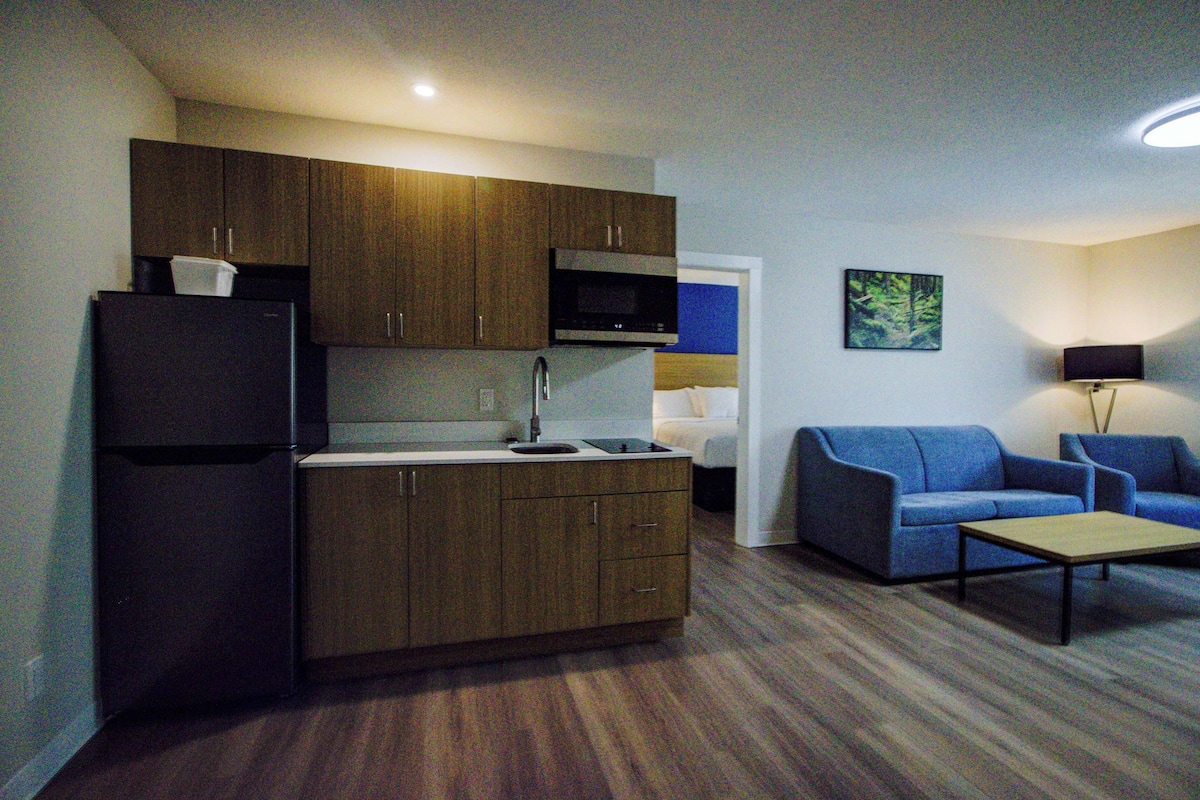 A compact living space with a kitchenette, a sofa, a coffee table, and a painting on the wall.