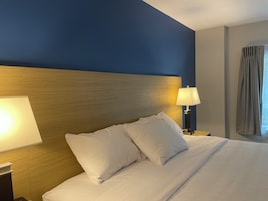 Una habitación de hotel con una cama grande, dos lámparas de noche y un ventanal con cortinas.