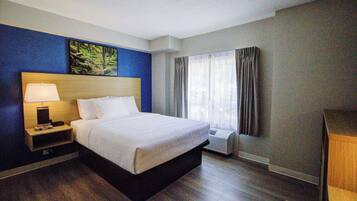 Habitación de hotel con cama, mesita de noche, lámpara, equipo de aire acondicionado y una ventana con cortinas.