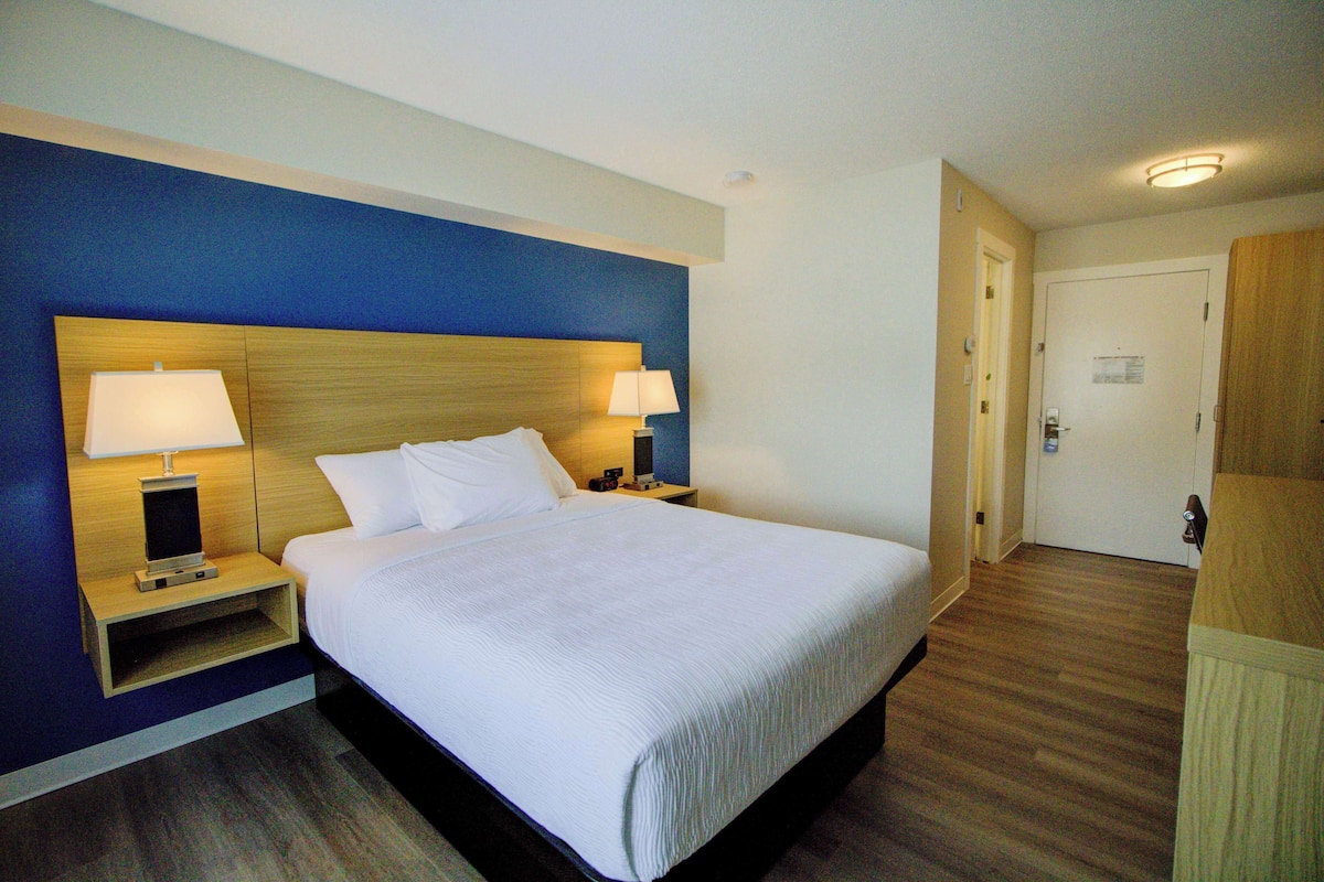 A hotel room with a large bed, two bedside tables with lamps, a wooden headboard, and a door to the right.