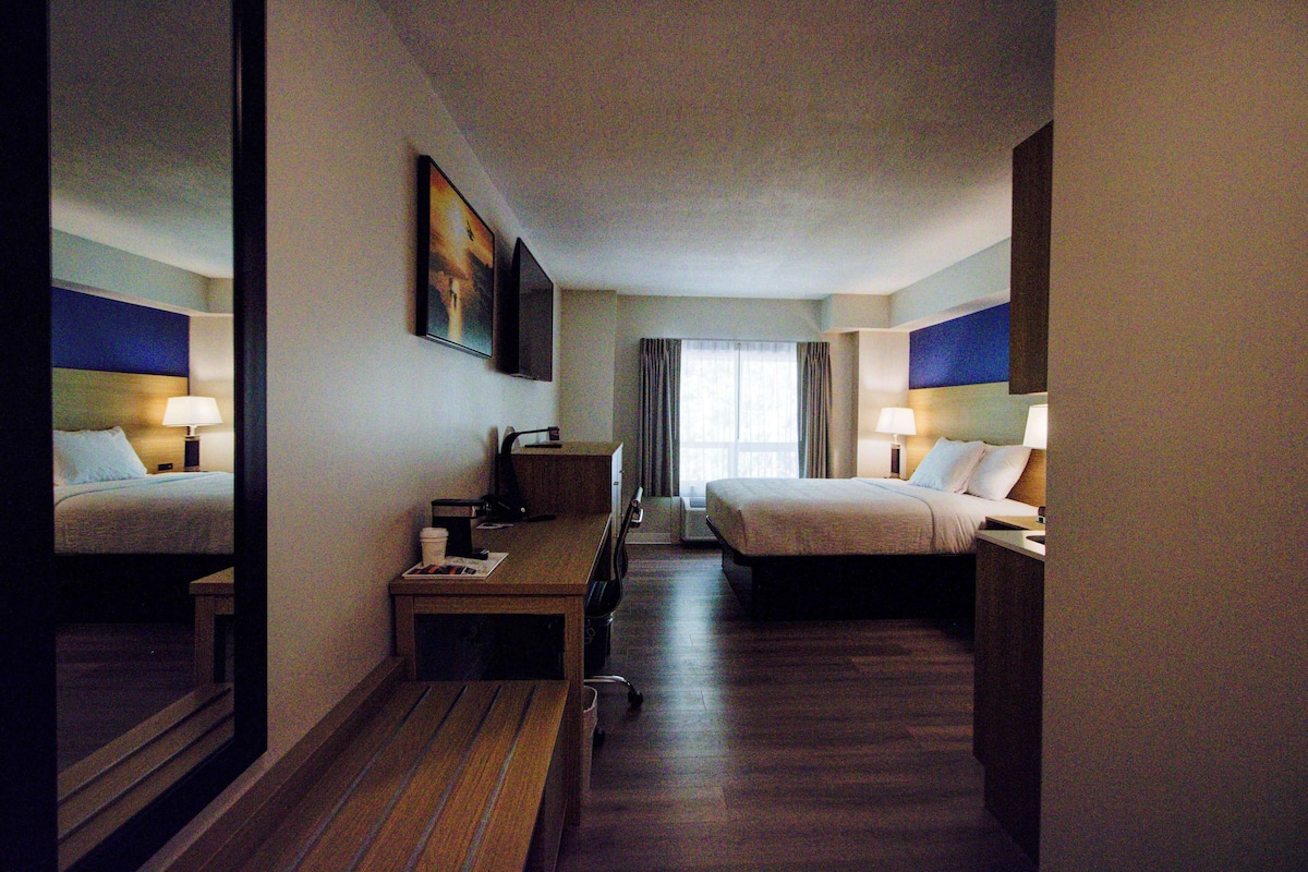 A hotel room with two beds, a desk, a chair, a mirror, and a window with curtains.