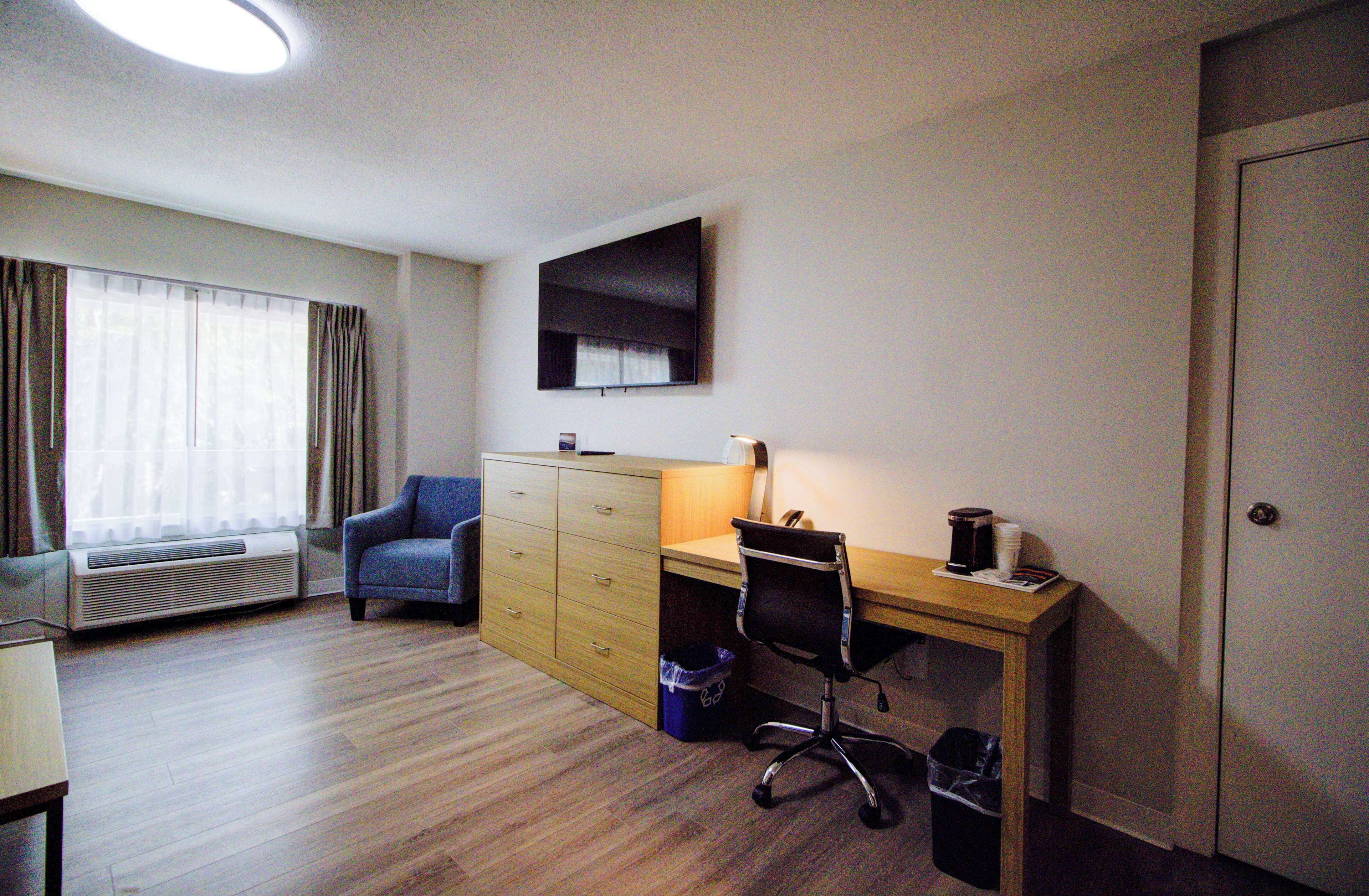 A hotel room with a wooden desk, a chair, a wardrobe, a heater, and a window with curtains.