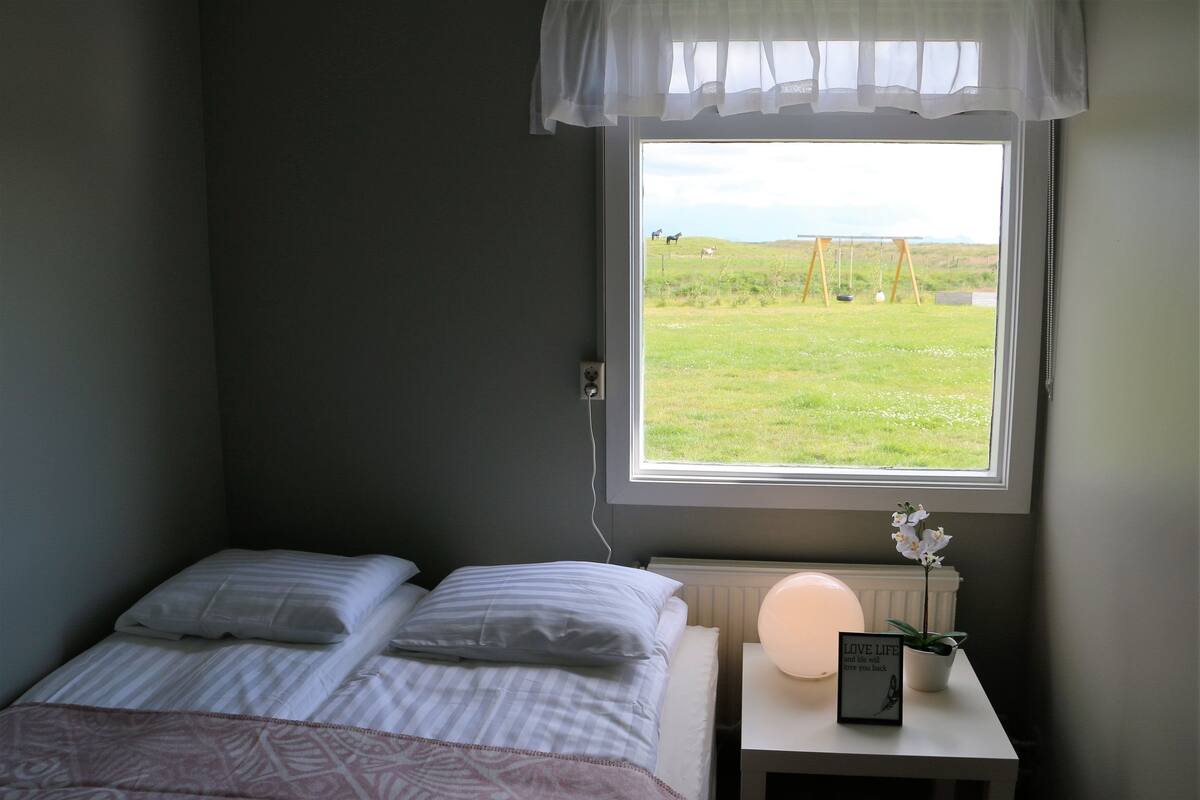 Une chambre à coucher avec un lit, une table de chevet avec une lampe et une fenêtre donnant sur un champ verdoyant et un portique.