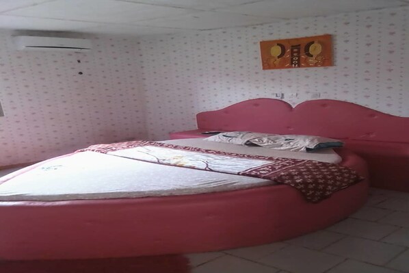 A room with a pink bed, patterned wallpaper, and a wall-mounted air conditioner. - Hôtel Ixora Diégonefla (Diégonéfla)