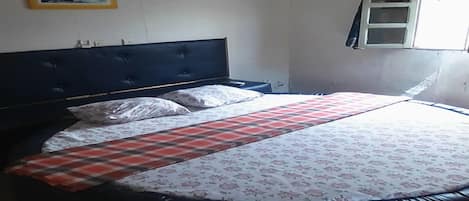 Een bed met een bloemenbedekking en een geruite deken, een donker hoofdeinde en een wandplank met een ingelijste foto.