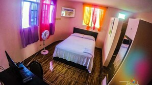 Una habitación de hotel con cama, escritorio con computadora, ventilador y cortinas en las ventanas.