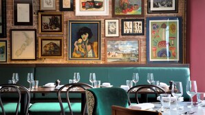 Ein Restaurant mit grünen Sitzbänken, gerahmten Kunstwerken an den Wänden und Tischen, die mit Gläsern und Besteck gedeckt sind.