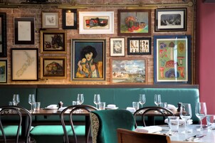 A restaurant with green upholstered booths, framed artwork on the walls, and tables set with glasses and cutlery.