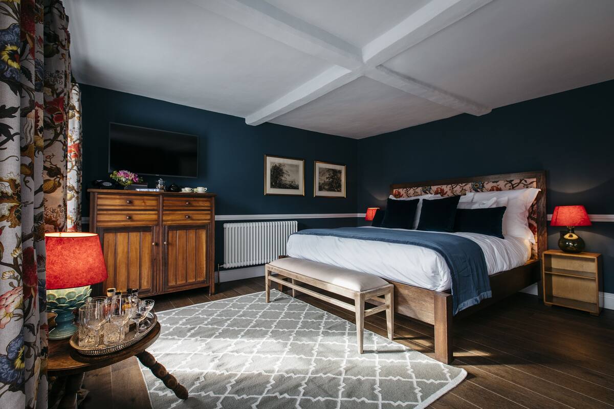 Une chambre à coucher comprenant un lit, des tables de chevet en bois, une commode, un radiateur et un téléviseur.