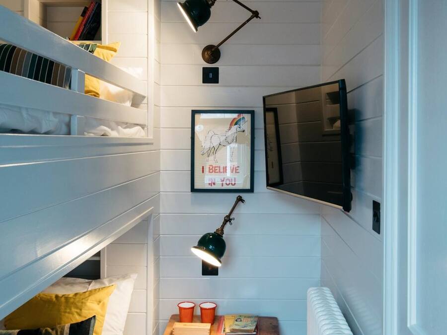 Une petite pièce étroite avec des lits superposés, une petite table avec des tasses et des livres, une affiche encadrée et un radiateur.