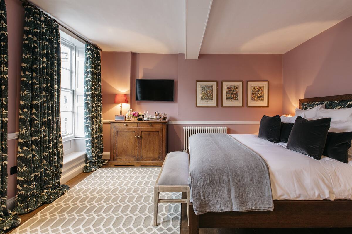 Une chambre à coucher avec un lit, une table de chevet, une lampe et une œuvre d’art accrochée au mur.