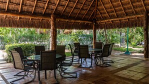 A covered outdoor seating area with tables and chairs, surrounded by greenery. - Condo Santuario by Playa Paradise (Playa del Carmen)