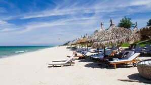 A beach with thatched umbrellas and sun loungers. - The Blue Alcove (Da Nang)