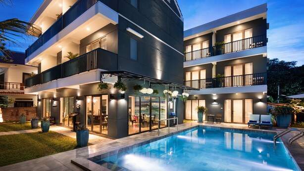 A modern multi-story building with a swimming pool, outdoor seating, and a well-lit entrance. - The Blue Alcove (Da Nang)
