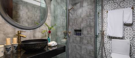 Une salle de bain moderne avec une douche à parois de verre, un miroir rond, un lavabo sur pied noir et des toilettes.