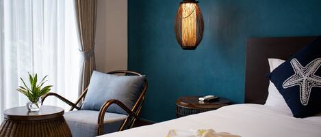 A hotel room with a bed, a chair, a round table with a plant, a hanging light fixture, and a wall with a starfish pillow.