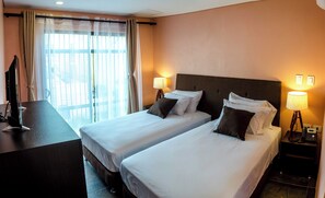 Quarto de hotel com duas camas, uma mesa, televisão e luminárias.