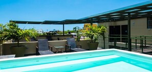 Uma área de piscina no terraço com vista desobstruída da linha do horizonte da cidade, cercada por espreguiçadeiras e plantas em vasos.