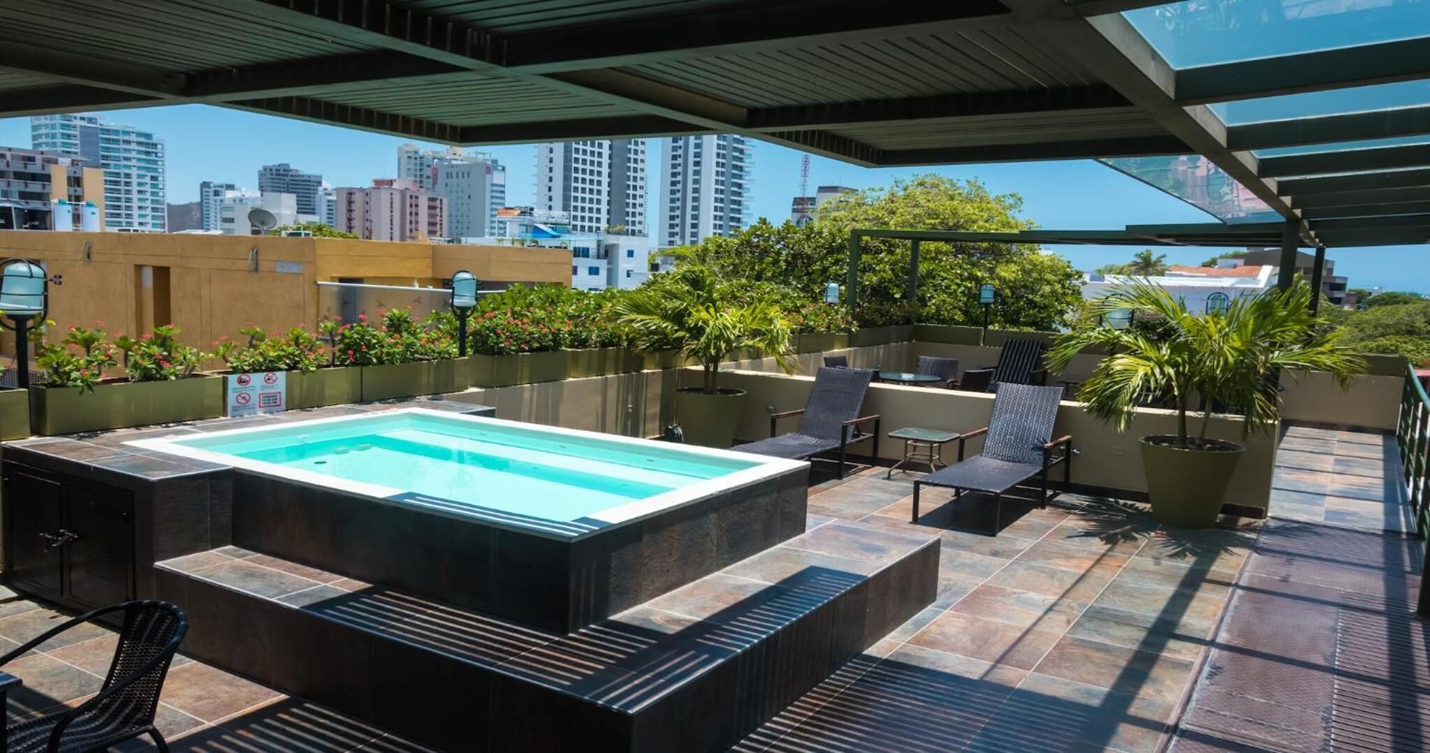 Un área de piscina en la azotea con jacuzzi, sillones de descanso y plantas en macetas.