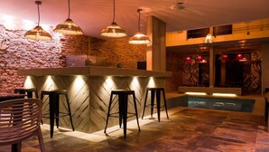 Zona de bar con pared de piedra, piscina e iluminación colgante.