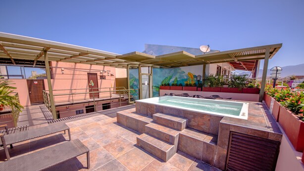 Un área de piscina en la azotea con un jacuzzi, mobiliario exterior y un mural.