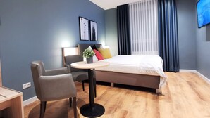 A modern hotel room with a bed, a desk, a chair, and a small table. - Hotel Restaurant Verst (Gronau (Westphalia))