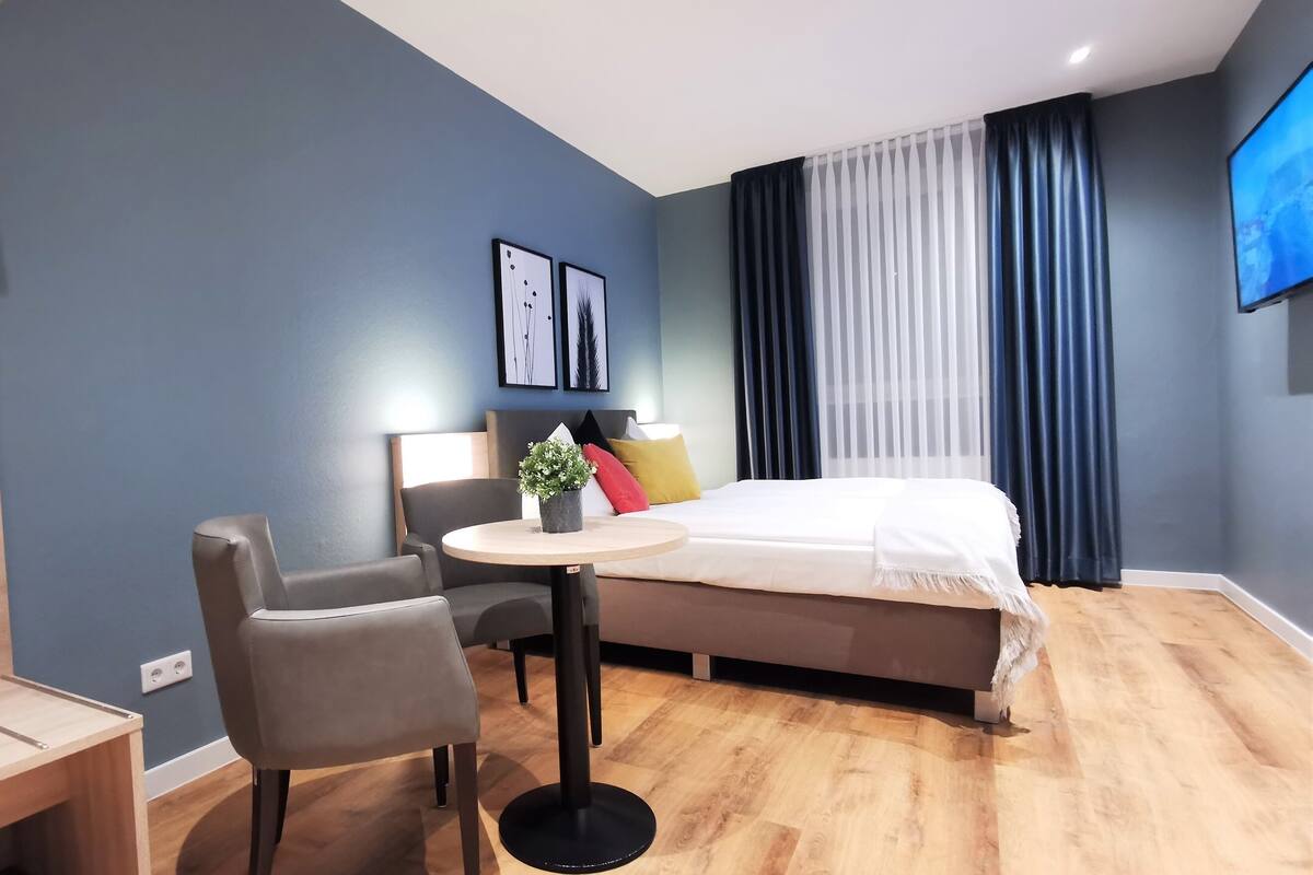 A modern hotel room with a bed, a desk, a chair, and a small table.