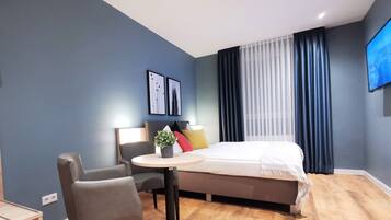 Relax in a stylish room with a comfortable bed, sofa, and potted plant, plus a large window and flat-screen TV.