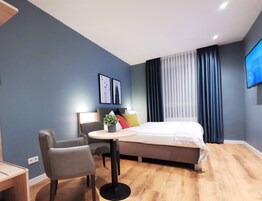 A modern hotel room with a bed, a desk, a chair, and a small table.