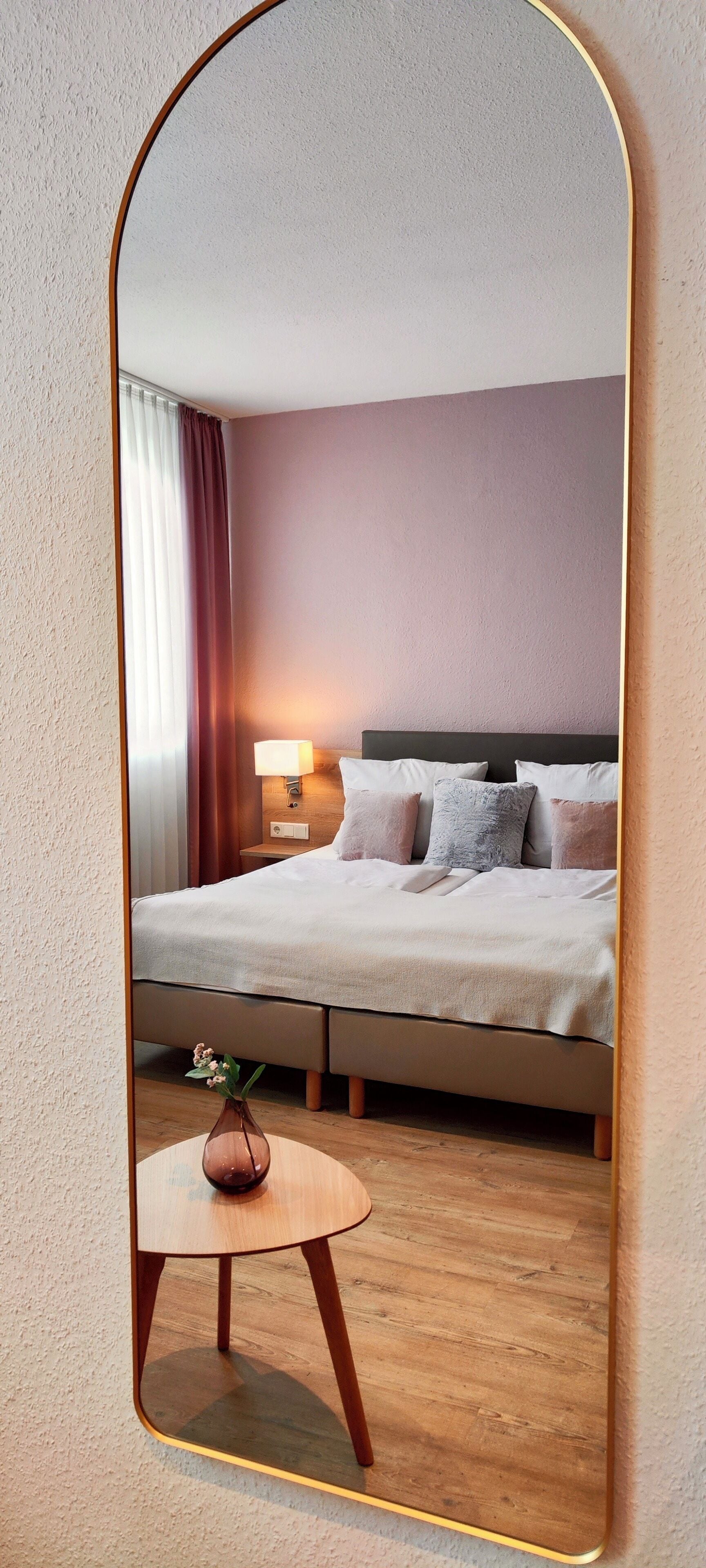 A hotel room with a bed, bedside table, lamp, and a vase with flowers.