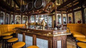 A bar area with wooden bar counter, stools, and large windows with stained glass. - Hotel Restaurant Verst (Gronau (Westphalia))