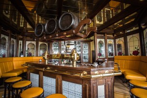 A bar area with wooden bar counter, stools, and large windows with stained glass.
