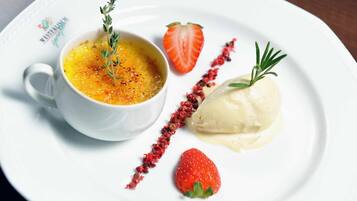 Un plato de postre con crema brûlée, una fresa y una cucharada de crema con una ramita de romero.