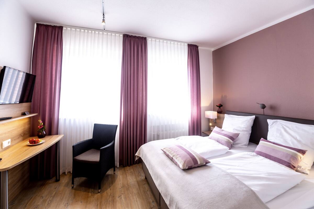 A hotel room with a bed, a desk, a chair, and a television.