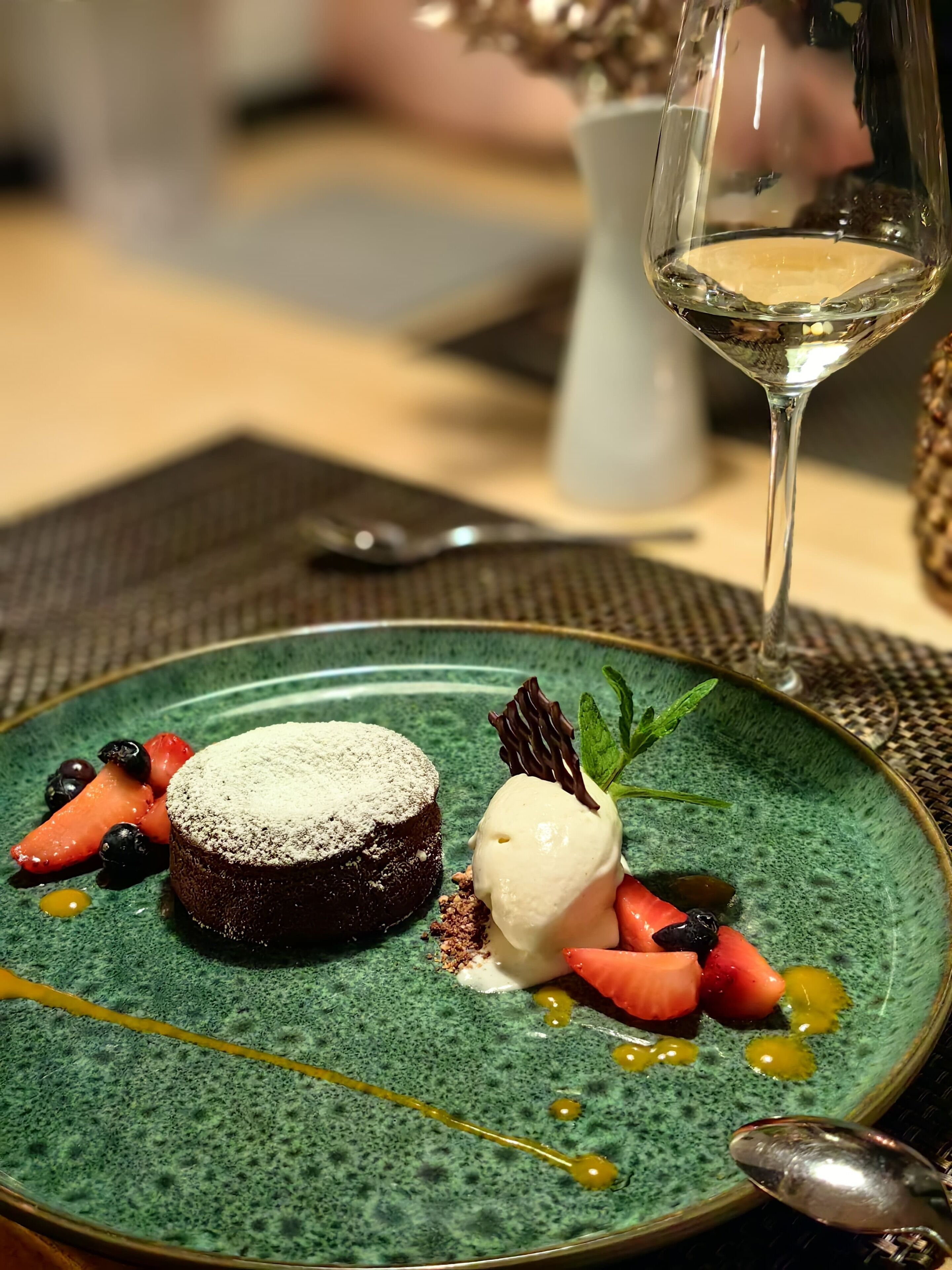 A dessert plate with a chocolate cake, ice cream, and fresh berries, accompanied by a glass of white wine.