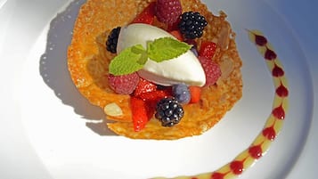 A dessert plate with a fruit-topped crepe, a dollop of cream, and a decorative sauce on the side.