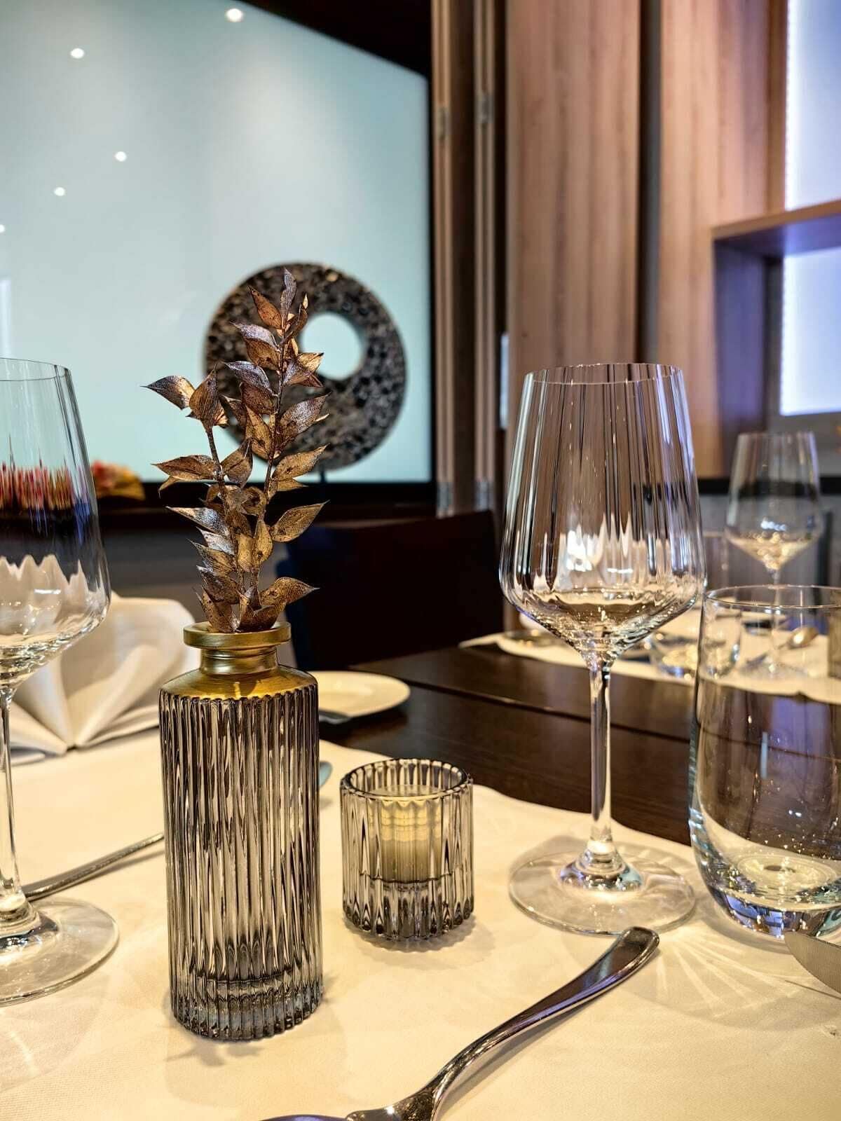 A dining table set with wine glasses, a decorative vase, and a candle holder.